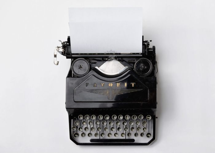 Alte Schreibmaschine der Marke Favorit vor weißem Hintergrund, ein weißes Blatt ist eingespannt, auf dem der Text beginnt "The revolution will be monospaced"