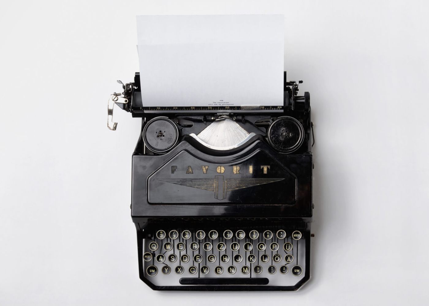 Alte Schreibmaschine der Marke Favorit vor weißem Hintergrund, ein weißes Blatt ist eingespannt, auf dem der Text beginnt "The revolution will be monospaced"