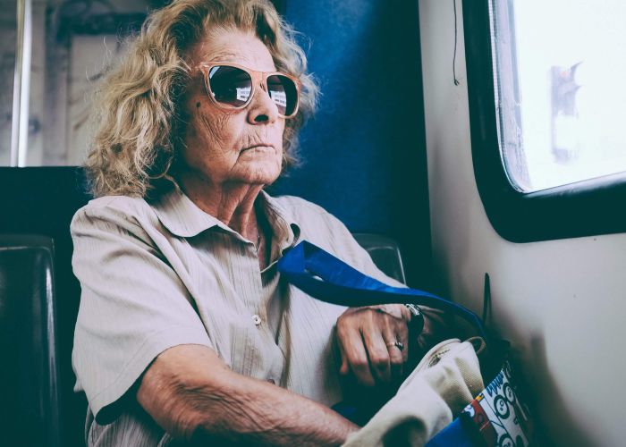 Ältere Dame mit Sonnenbrille sitzt in einem Zug und greift in ihre Tasche