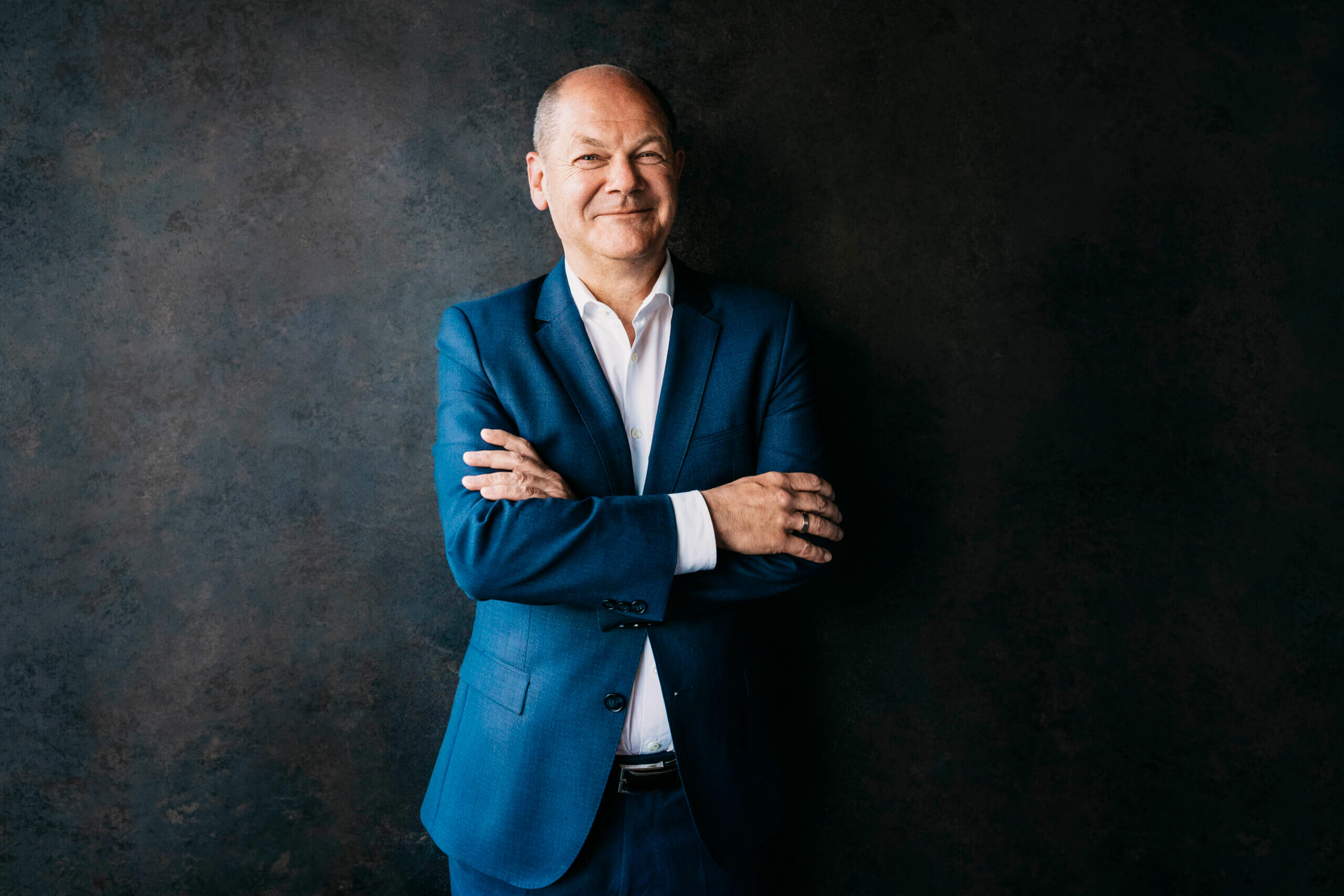 Zuversichtlich lächelnder Olaf Scholz vor dunklem Hintergrund in blauem Anzug, Portrait fotografiert von Anne Hufnagl