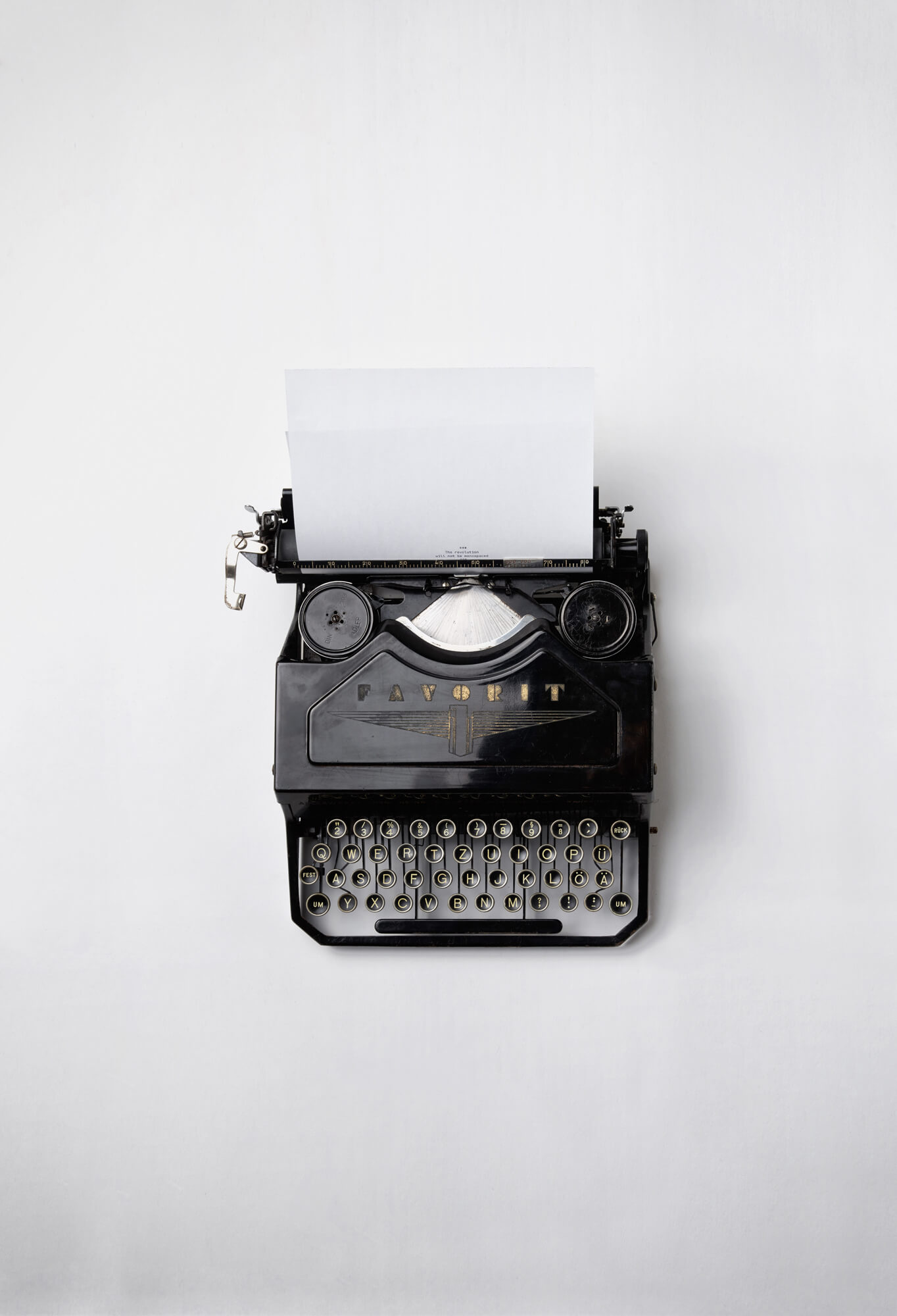 Alte Schreibmaschine der Marke Favorit vor weißem Hintergrund, ein weißes Blatt ist eingespannt, auf dem der Text beginnt "The revolution will be monospaced"