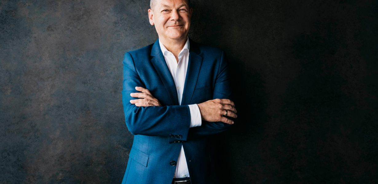 Zuversichtlich lächelnder Olaf Scholz vor dunklem Hintergrund in blauem Anzug, Portrait fotografiert von Anne Hufnagl